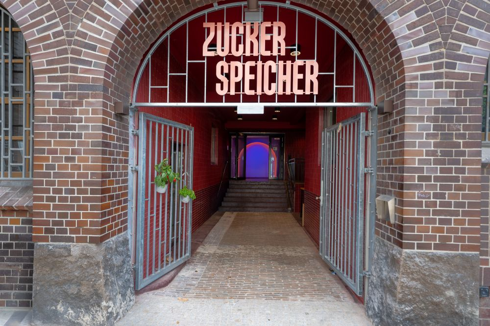 Sanierter Torbogen-Eingang mit Neon-Schriftzug Zucker Speicher